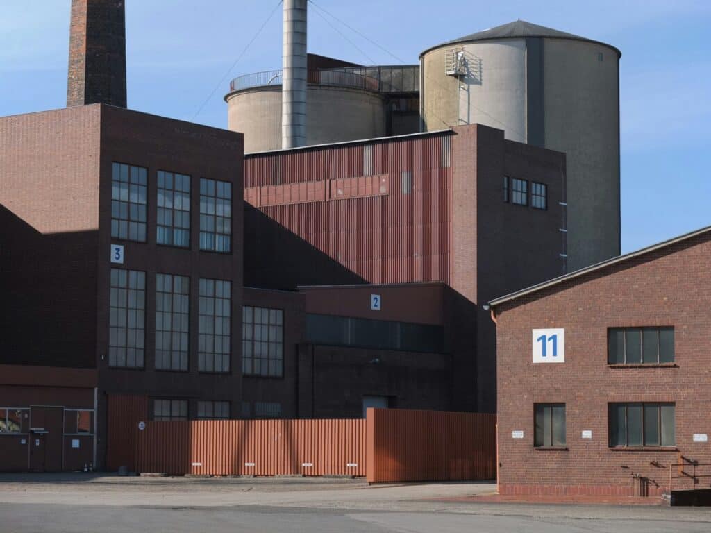 Modern industrial building with brick and metal siding, large factory silos, and numbered warehouse units under a clear blue sky.