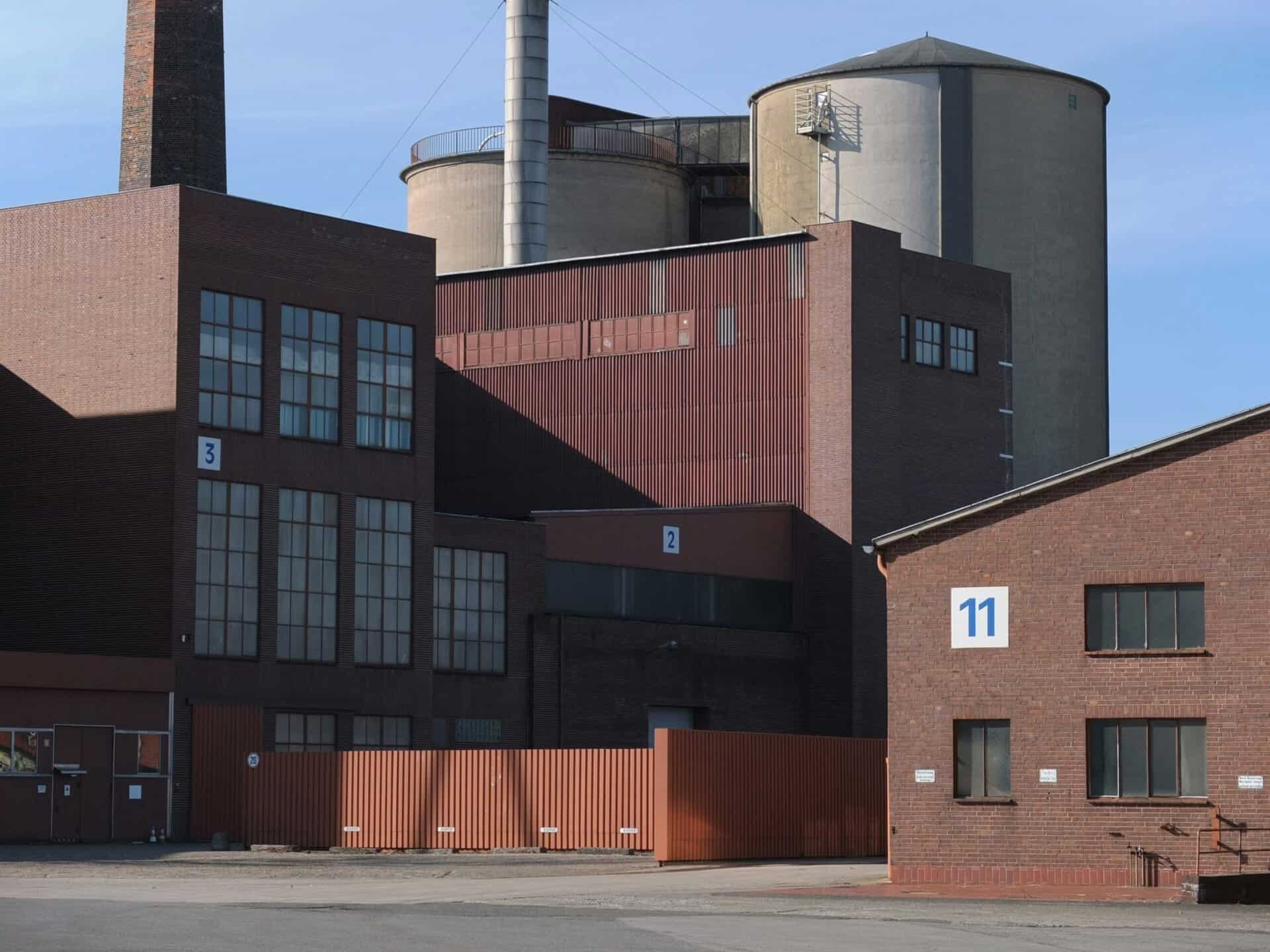Modern industrial building with brick and metal siding, large factory silos, and numbered warehouse units under a clear blue sky.